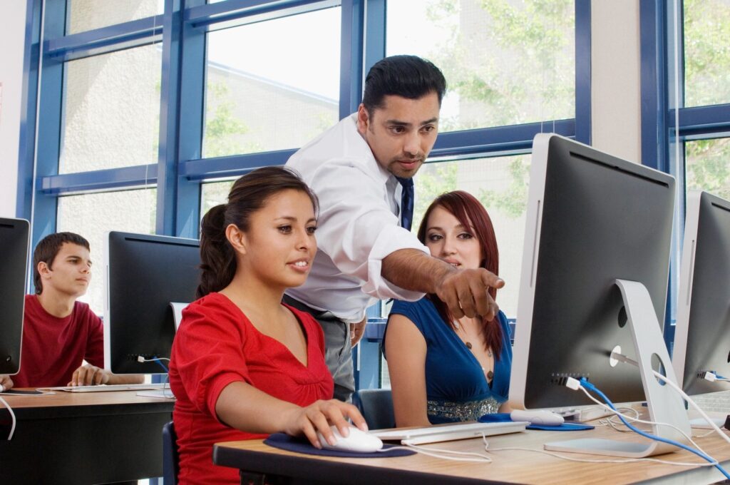A man guides two women working on a computer in an office.