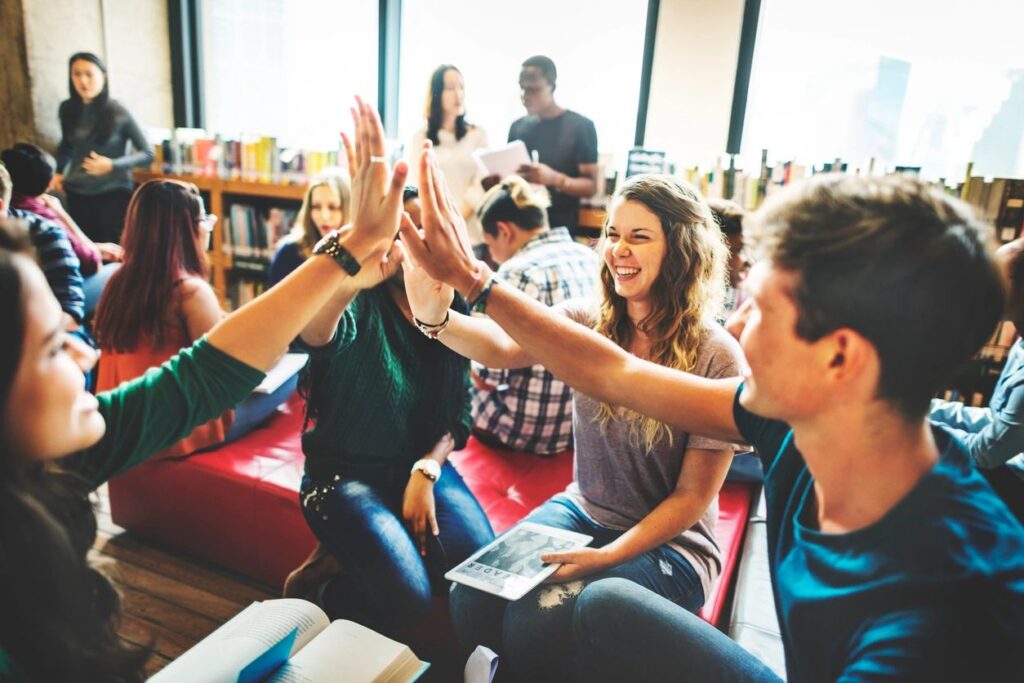 Group of young adults happily giving high fives indoors.